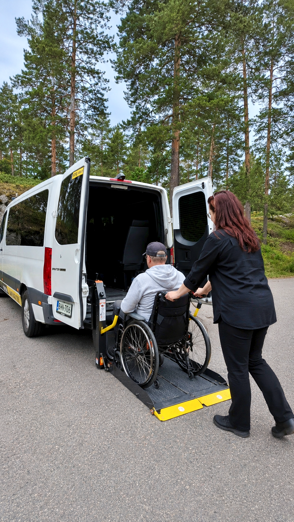 Kuljettaja avustaa pyörätuoliasiakkaan turvallisesti invataksin hissille